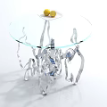 Circular Glass Top Coffee Table With Silver Sculptural Base And Yellow Fruits On Plate