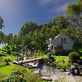 Sunlit Scenic White House in Woods with Stream Wooden Bridge Grass and Wildflowers Green Hills