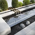 Modern Water Fountain Design With Metal Spouts Flowing Water Pebbles Green Shrubs And Stone Slabs