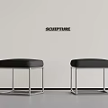 White Wall With Sculpture Sign And Two Black Leather Metal Frame Stools On Gray Floor