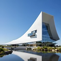 Modern Cultural Center Building Featuring Streamlined White Roof Glass Curtain Walls Water Reflection And Greenery