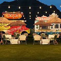 Garden Landscape With Food Trucks Green Grass Outdoor Seating String Lights Mountain Backdrop In Evening