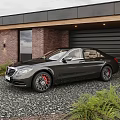 Black Luxury Sedan with Red Brake Calipers Parked at Brick Wall Garage on Gravel Driveway