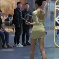 Woman In Yellow Open Back Dress Holding Small Object In Outdoor Crowd Scene