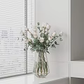 White Roses With Greenery In Transparent Golden Frame Vase On White Cabinet By Window Blinds