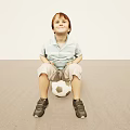 Young Boy Sitting On Soccer Ball In Light Colored Room With Striped Shirt And Sneakers