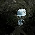 Natural Cave Entrance View with Flowing Stream and Overcast Sky like Lush Vegetation and Rocks