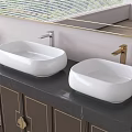 Two White Above Counter Washbasins With Gold Silver Faucets On Black Countertop And Dark Cabinets