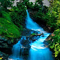 Scenic Natural Waterfall Scene With Flowing Blue Water Lush Green Vegetation And Rocks