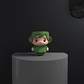 Green Cartoon Character Shaped Mug On Gray Round Platform With Black Wall And Brown Stirrer
