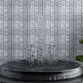 Garden Ornament Featuring Circular Fountain With Water Splashing Against Gray Striped Wall And Green Shrubs