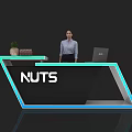 Modern Exhibition Reception Desk With Blue Accents NUTS Logo Laptop Books Plant And Receptionist