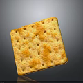 Golden square cracker with small holes and orange spots showing surface texture on gray background