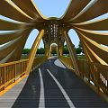 Yellow Arch Structure Bridge With Wooden Deck Railings Blue Sky And Trees