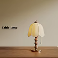 Table lamp with wooden base metal accents and light colored petal lampshade on wooden table