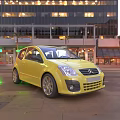 Yellow Citroen Hatchback Parked On City Street With Modern Tall Buildings And Neon Lights