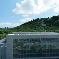 Bright Blue Sky With Fluffy White Clouds Over Lush Green Forested Hills Beside Modern Building