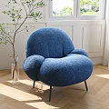 Blue Plush Rounded Lounge Chair With Black Metal Legs In Bright Room With Green Plant