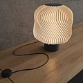 Modern Wavy Lampshade Table Lamp With Warm Light On Wooden Table Against Gray Wall