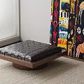 Black Leather Ottoman With Diamond Stitching And Wooden Base On Carpet Near Colorful Abstract Painting