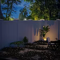 Serene Nighttime Outdoor Space With White Fence Stone Patio Green Plants And Striped Chair
