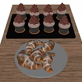 Tray Of Cupcakes With Chocolate Frosting And Plate Of Powdered Sugar Croissants On Wooden Table