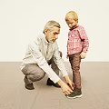 Elderly Man And Young Boy Tying Shoelaces Together In Indoor Setting With Light Wall And Gray Floor