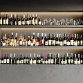 Neatly Arranged Wine Bottles And Glasses On Multi Layer Display Shelves With Gray Wall