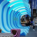 Surfing Themed Illuminated Wave Structure With People Taking Photos In Urban Night View