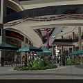 Outdoor Shopping Mall Area With Green Umbrellas Shops People And Decorative Arch