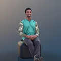 Man In Green Shirt With Camouflage Sleeves Sitting On Black Stool Hands Clasped Gray Background
