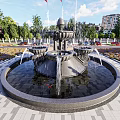 Ornate Fountain With Central Sculpture Water Flowing In Urban Plaza With Buildings And Greenery