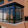 Glass Sunroom Attached To Red Brick Building With Black Frame And Glass Windows