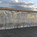 Building Exterior Wall With Thatched Roof And Peeling Gray Yellow Patches Against Sky And Water