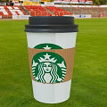 Starbucks Coffee Cup With Green Logo Brown Sleeve And Black Lid On Green Grass Field