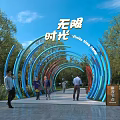 Pergola With Blue And Red Curved Structures Surrounded By Green Trees And People Walking