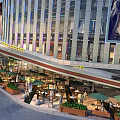 Modern Commercial Street Featuring Glass Facades Outdoor Dining Green Umbrellas And Pedestrians