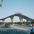 Modern Arched Entrance Gate With LOGO Sign Vehicles Passing By And Green Trees Around