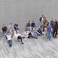Group of People Sitting and Standing in Modern Space with Gray Wall and Tiled Floor