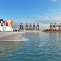 Fully Loaded Container Ship Sails Near Busy International Commercial Seaport With Large Port Gantry Cranes