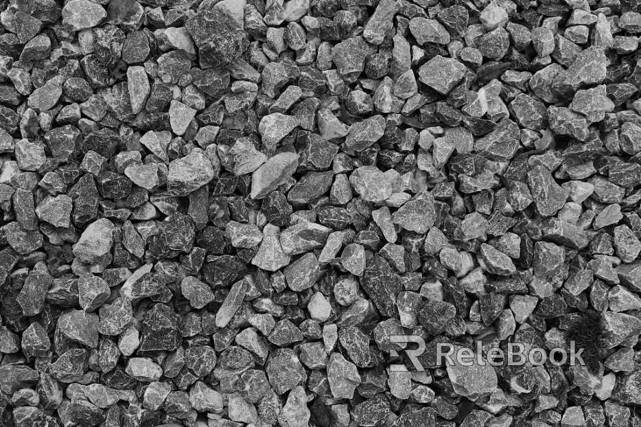 The image depicts a close-up of gravel, showcasing an array of small, irregularly shaped stones in various shades of gray, brown, and black, set against a contrasting light background.